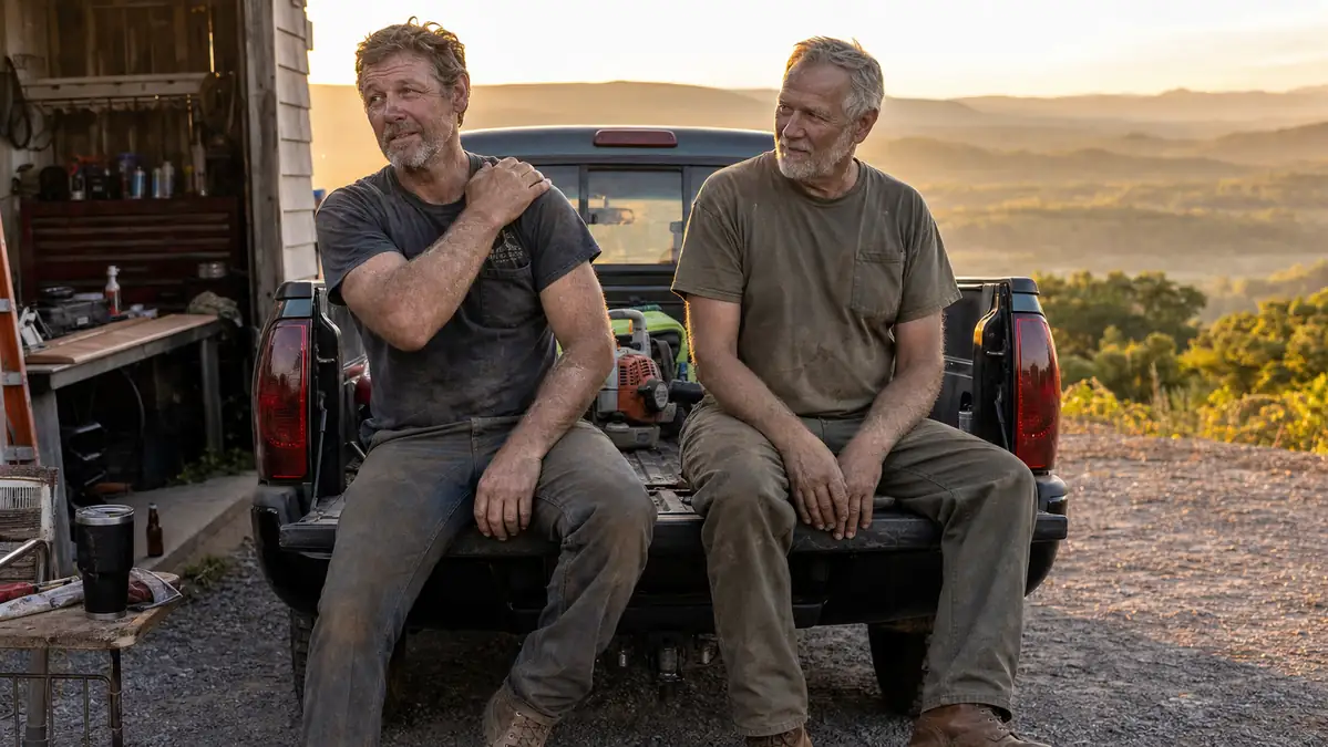 Two men in landscaping work clothes taking a water break by a truck at the end of a job